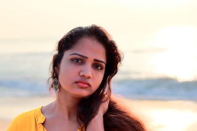 Portrait of beautiful woman at beach against sky during sunset