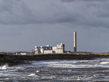 Factory by sea against sky