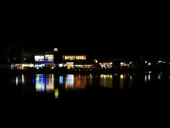 Illuminated city by river against sky at night