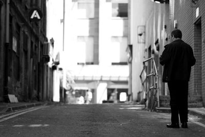 Rear view of man walking on street amidst buildings