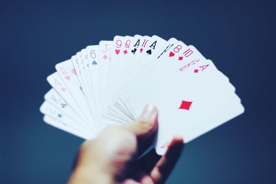 Cropped hand holding playing cards against blue background