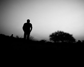 Rear view of silhouette man standing on field against clear sky