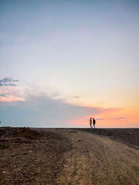 People walking at beach against sky during sunset