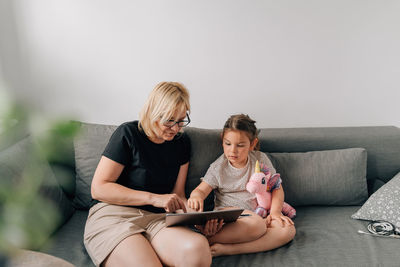 Woman with digital tablet sitting with granddaughter at home