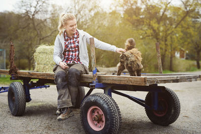 Smiling teenage girl stroking cat while sitting on old-fashioned trailer