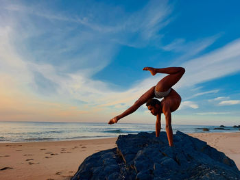 Full length of woman doing yoga at beach against sky during sunset