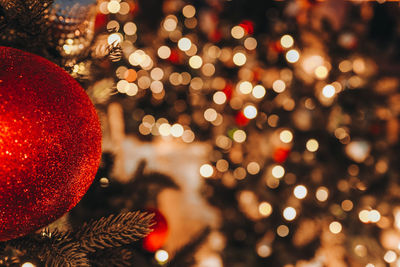 Christmas toy red ball hanging on the christmas tree with blurry golden festive bokeh lights