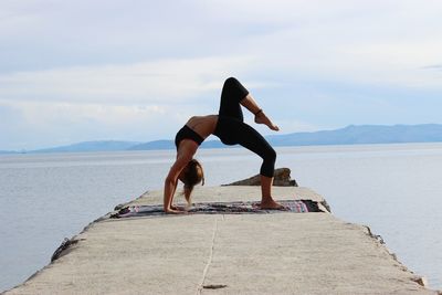 Full length of woman doing yoga on pier amidst sea