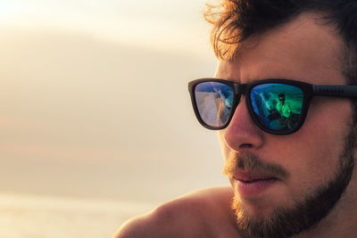 Close-up of man wearing sunglasses against sky during sunset