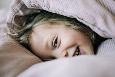 Close up candid portrait of girl in bed smiling hiding in the covers