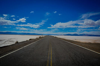 Empty road by landscape against blue sky