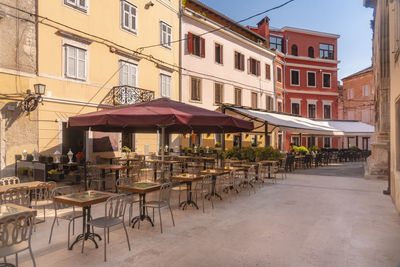 Chairs and tables at sidewalk cafe by buildings in city