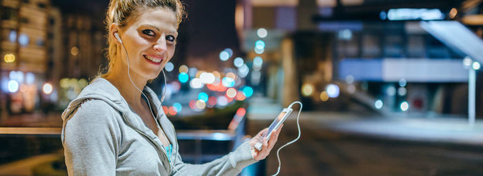 Portrait of smiling young blonde sportswoman listening music on mobile phone application