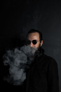 Man exhaling smoke against gray wall