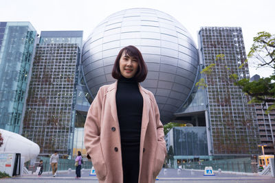 Portrait of smiling young woman standing against buildings in city