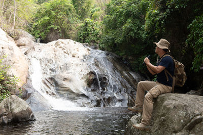 Man sitting on rock by river in forest