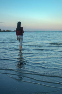 Rear view of woman standing in sea against clear sky