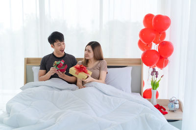 Rear view of man and woman holding balloons at home