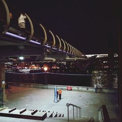 People on illuminated bridge at night