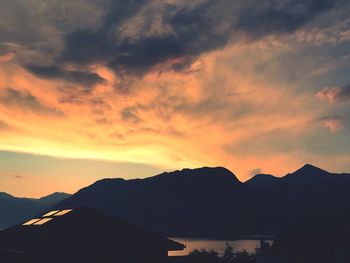 Silhouette houses and mountains against dramatic sky during sunset