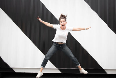 Full length of cheerful woman jumping against wall 