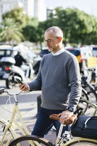 Businessman using smart phone while standing by bicycle in city