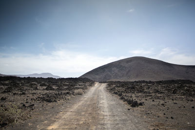 Dirt road leading towards mountains against sky