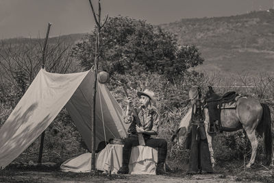 Woman sitting by tent by horse against mountain