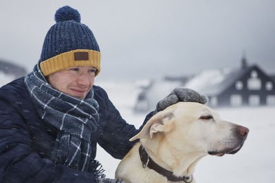 Man dressed in a warm clothing stroking his dog enjoying snowing. pet owner and labrador in winter.