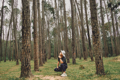 Full length of woman sitting on tree trunk in forest