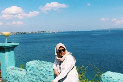 Portrait of smiling young woman by sea against sky