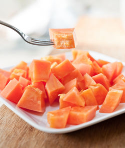 Cropped image of fork with papaya in plate on table