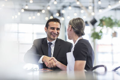 Businessman giving handshake to female chef at table in restaurant