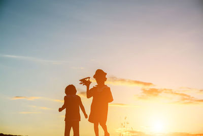 Rear view of friends with arms outstretched against sky during sunset