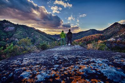 Rear view of people standing on mountain against cloudy sky