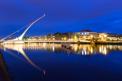 Illuminated buildings by river against sky at night