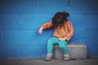 Full length of girl sitting against blue wall