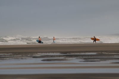 People walking on shore at beach against sky