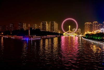 Illuminated city by river against sky at night