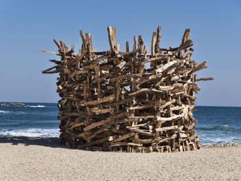 Stack of firewood on beach against clear sky