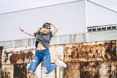 Full length of cheerful woman jumping against wall