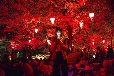 Low angle view of woman standing by illuminated tree at night