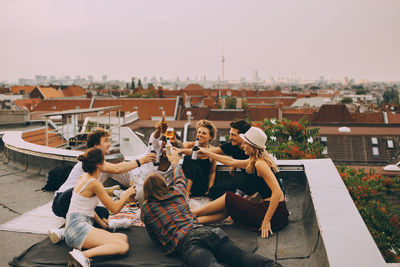 Cheerful friends toasting beer while relaxing on terrace at city