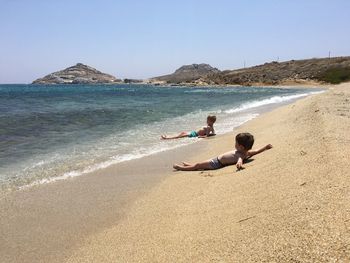 Boys enjoying at beach against sky on sunny day