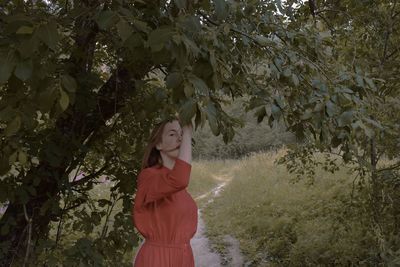 Young woman standing by tree against plants