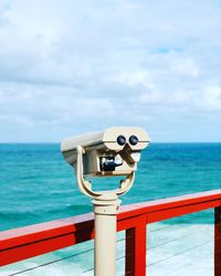 Coin-operated binoculars by sea against sky