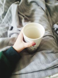 High angle view of hand holding coffee cup on bed warming up with hot drink 