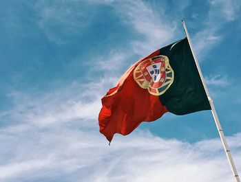 Low angle view of portuguese flag waving against blue sky
