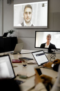 Male and female professionals discussing with team through video conference seen in meeting at office