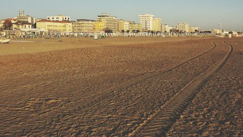 Tire tracks on beach by buildings against sky